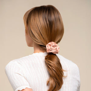 Person with long brown hair tied in a ponytail with a terracotta rosette ruched satin scrunchie, wearing a white shirt.
