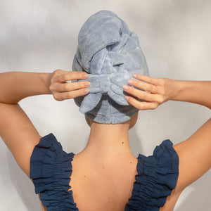 Back view of female model adjusting the bow detail on KITSCH Coastal Blue Plush Microfiber Hair Towel Turban — hands securing turban on head — lifestyle model shot — Ultra Absorbent, Made with Recycled Fabric — For all hair types & lengths