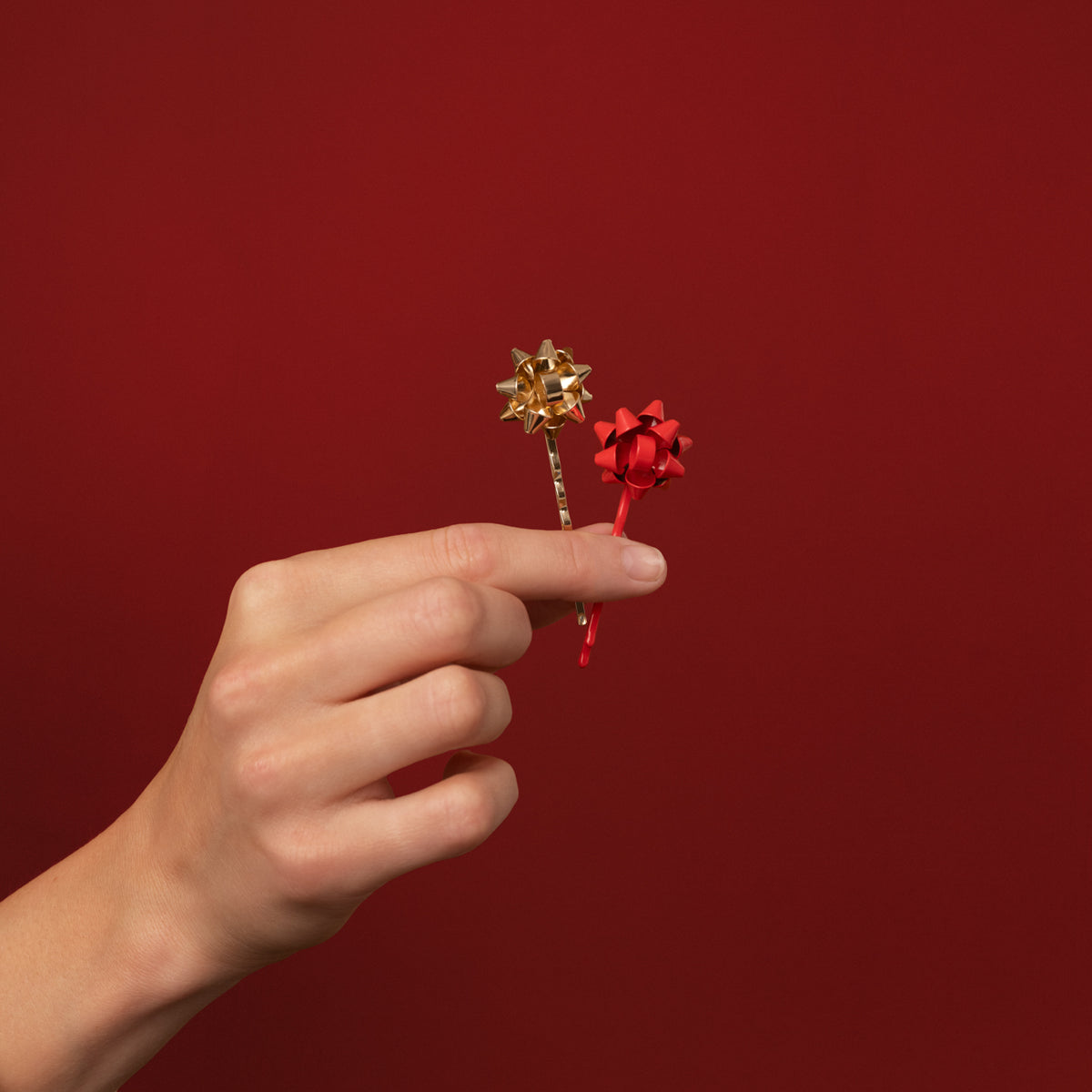 KITSCH Red & Gold Metal Gift Bow Bobby Pins 4pc Set — hand holding one gold and one red bow pin against a deep red backdrop — Merry red and gold hues add a fun touch to any look — holiday celebrations