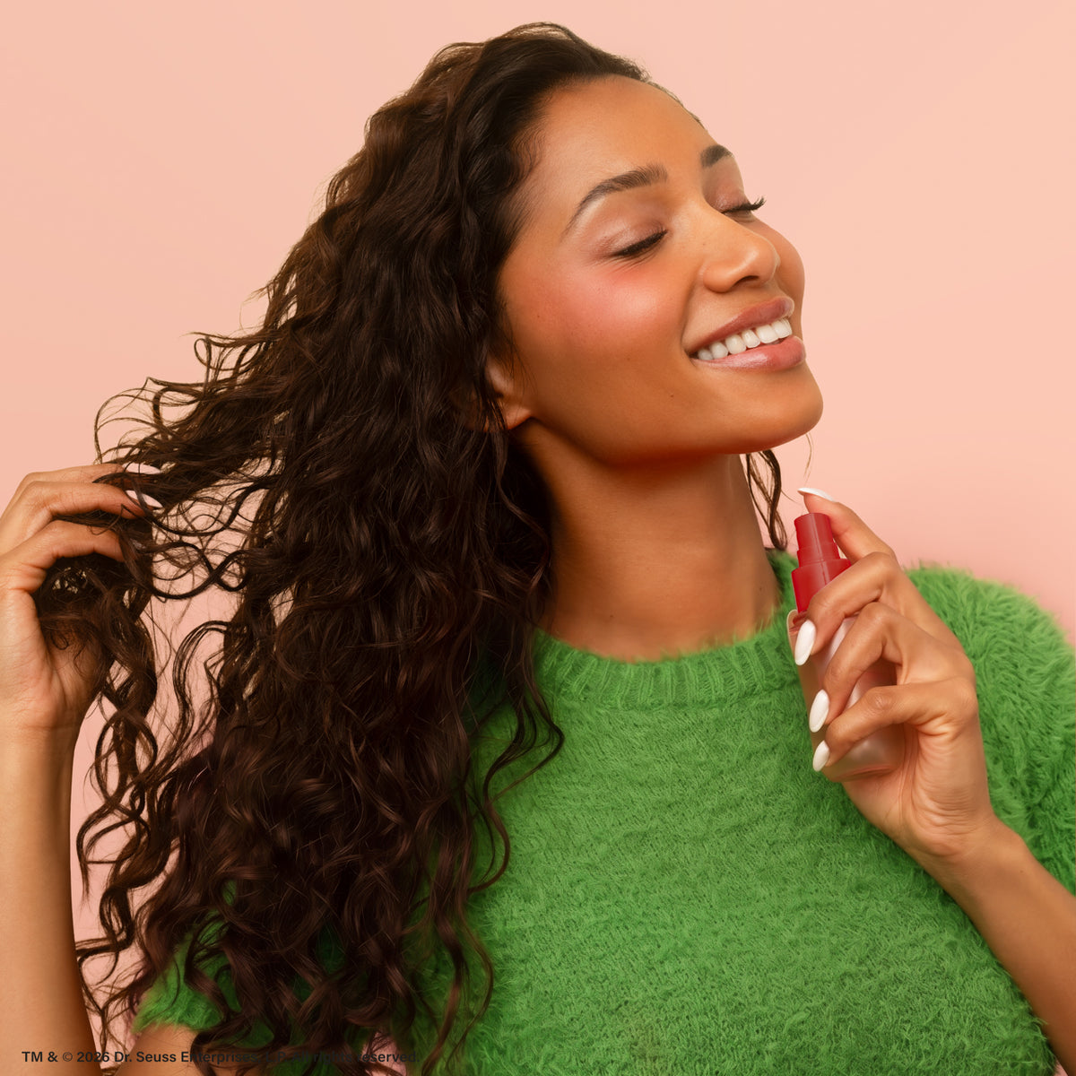 Model misting The Grinch x Kitsch Cherry Cheer Hair Perfume onto curly hair